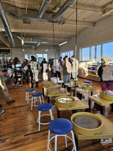 Ros O'Brien's Friendly City Clay and Art room located in the Manufactory Collective shows clay throwing wheels with blue stools next to them while people mingle in the space. locally, owned, handmade, handcrafted, harrisonburg, downtown, small, business, buy